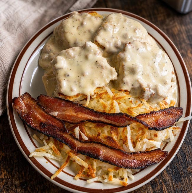 About Spiro’s All Day Diner: Plate with hash browns, bacon, and biscuits covered in creamy gravy.
