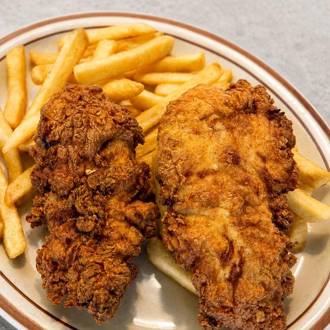 About Spiro’s All Day Diner: Two pieces of fried chicken with golden fries on a beige plate.